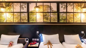 Une chambre d’hôtel avec deux lits, une grande fenêtre donnant sur la verdure et un luminaire fixé au mur.