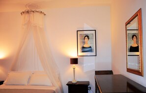 A bedroom with a bed, a bedside table with a lamp, a framed portrait, and a mirror on the wall. - Agriturismo Villa Toscana (Campiglia Marittima)