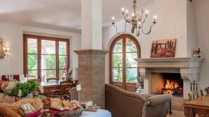 A dining area with a fireplace, wooden furniture, and a chandelier. - Agriturismo Villa Toscana (Campiglia Marittima)