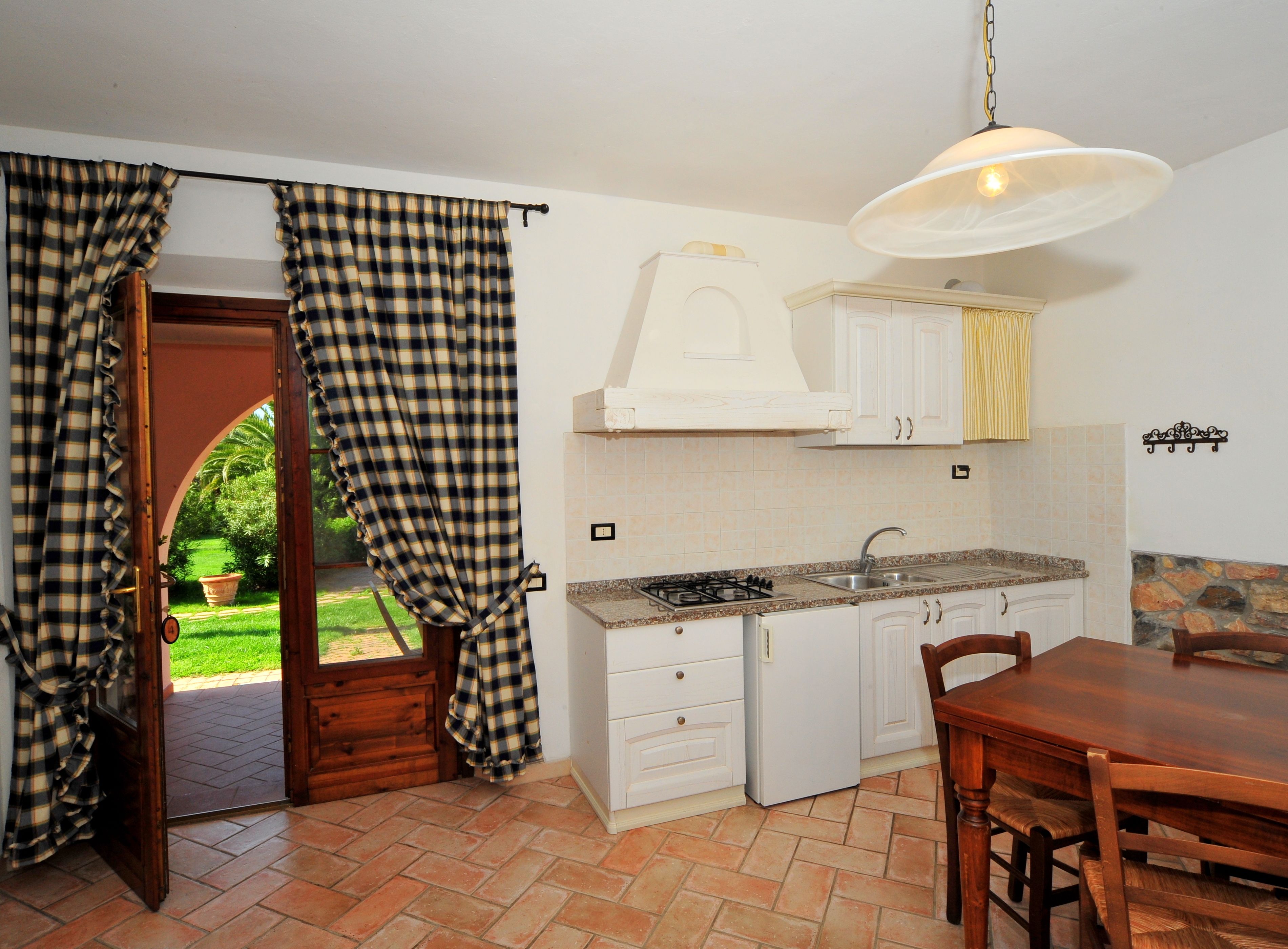 A kitchen with white cabinets, a stove, and a sink. There is a dining table with chairs and a hanging light fixture.