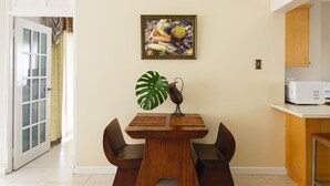 A dining area with a wooden table and chairs, a large green plant, and a framed picture on the wall.