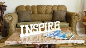 A living room with a sofa, a coffee table with 'INSPIRING' decor, and two wooden art pieces on the wall.
