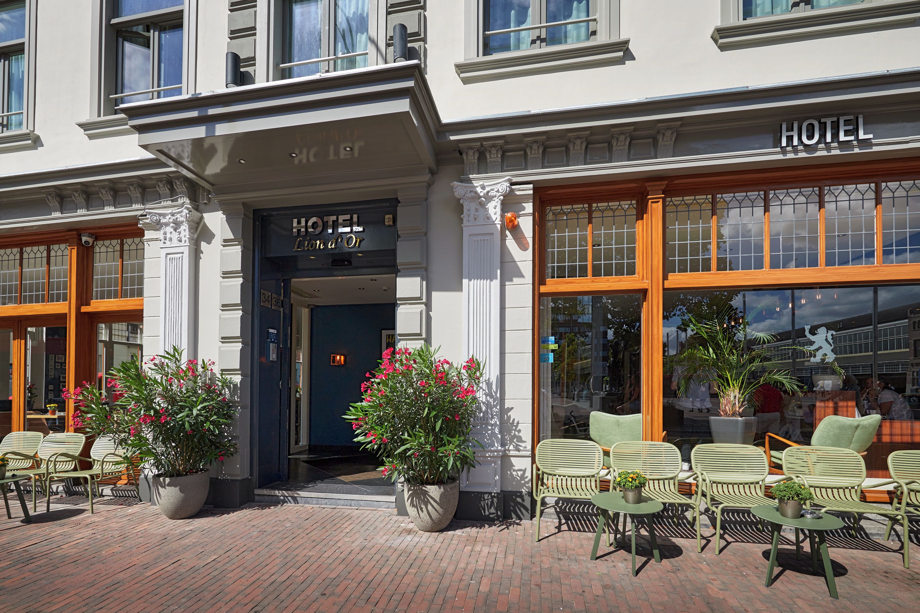 A hotel entrance with a sign reading 'HOTEL' and 'L'Hotel d'Or'. There are outdoor seating areas with chairs and potted plants.