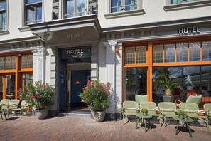 A hotel entrance with a sign reading 'HOTEL' and 'L'Hotel d'Or'. There are outdoor seating areas with chairs and potted plants. - Hotel Lion d'Or (Haarlem)