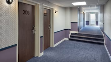 Corredor de hotel com duas portas identificadas com os números 306 e 307, piso coberto de carpete e escada que leva a outro andar.
