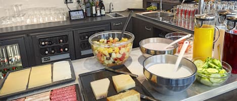 A buffet with various cheeses, meats, fruits, and beverages.