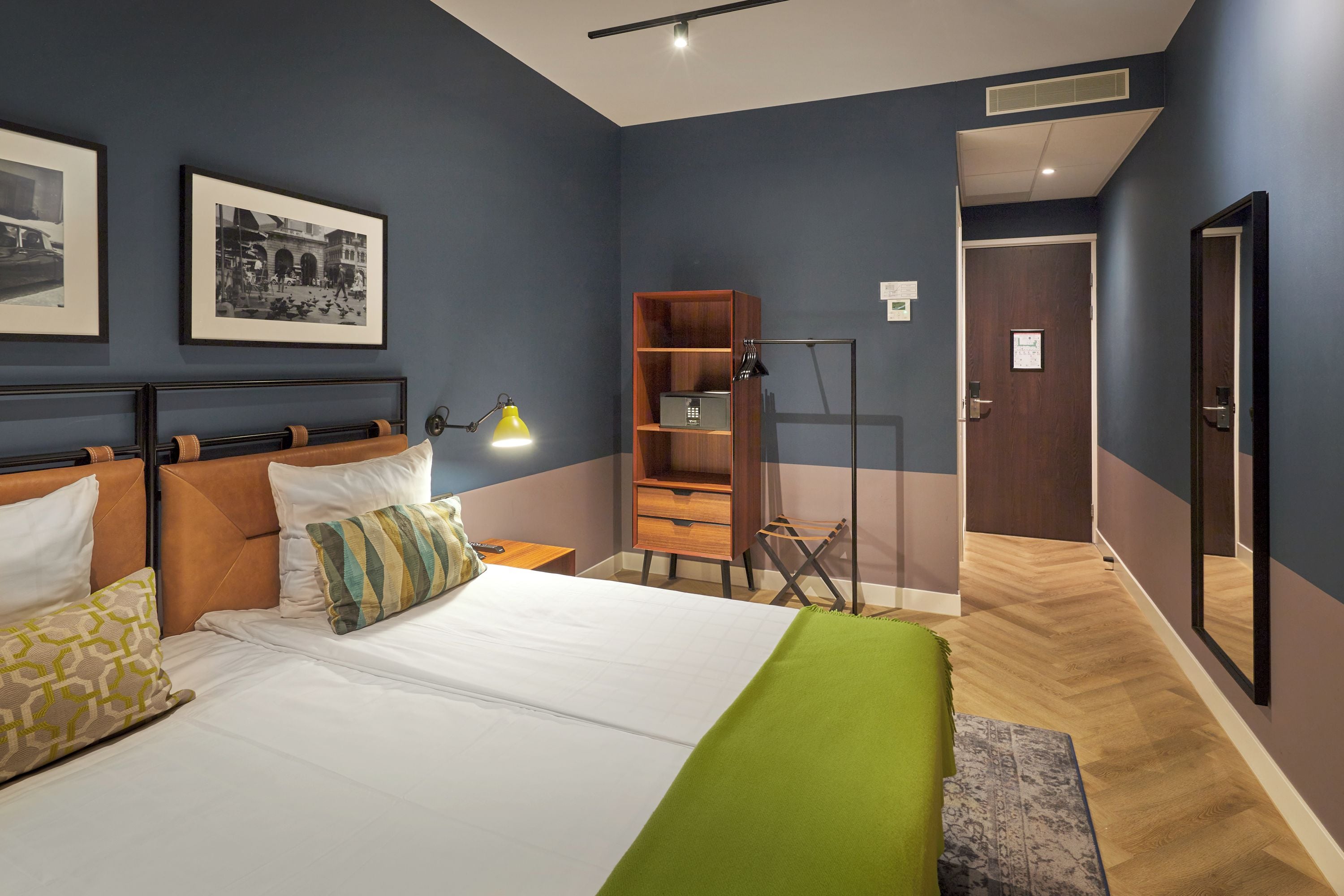 A hotel room with a bed, a desk, a bookshelf, and a door.