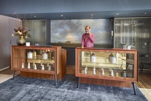 Zona de recepción con dos vitrinas de madera que exhiben objetos decorativos, un cuadro grande de un paisaje y una decoración de estilo moderno.