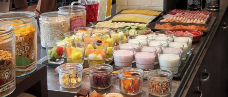 Un bufé con diversas opciones de comida, incluyendo frutas, quesos, carnes y pasteles.