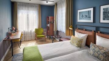 A hotel room with a bed, a desk, a chair, a wardrobe, and two framed pictures on the wall.