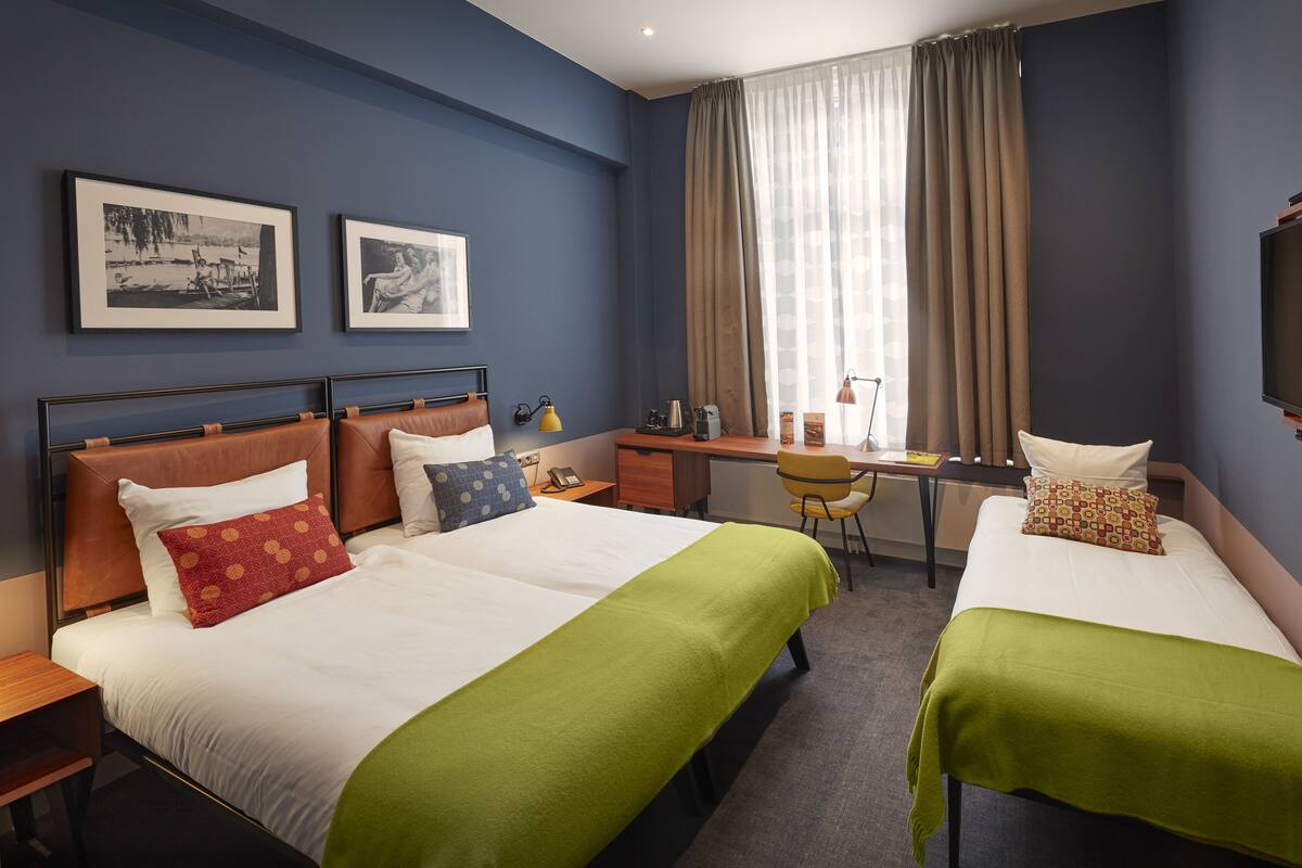 A hotel room with two beds, a desk, a chair, and a TV.