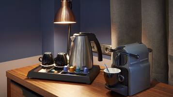 A kitchenette with a coffee maker, kettle, and cups on a wooden countertop.