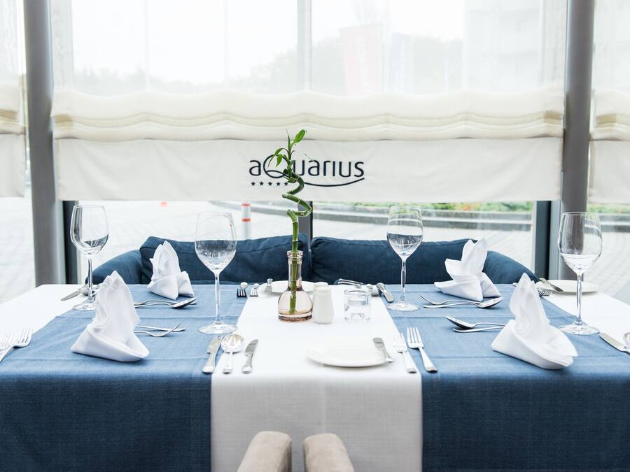 A table set for two with a blue tablecloth, white napkins, and a vase with a green plant.