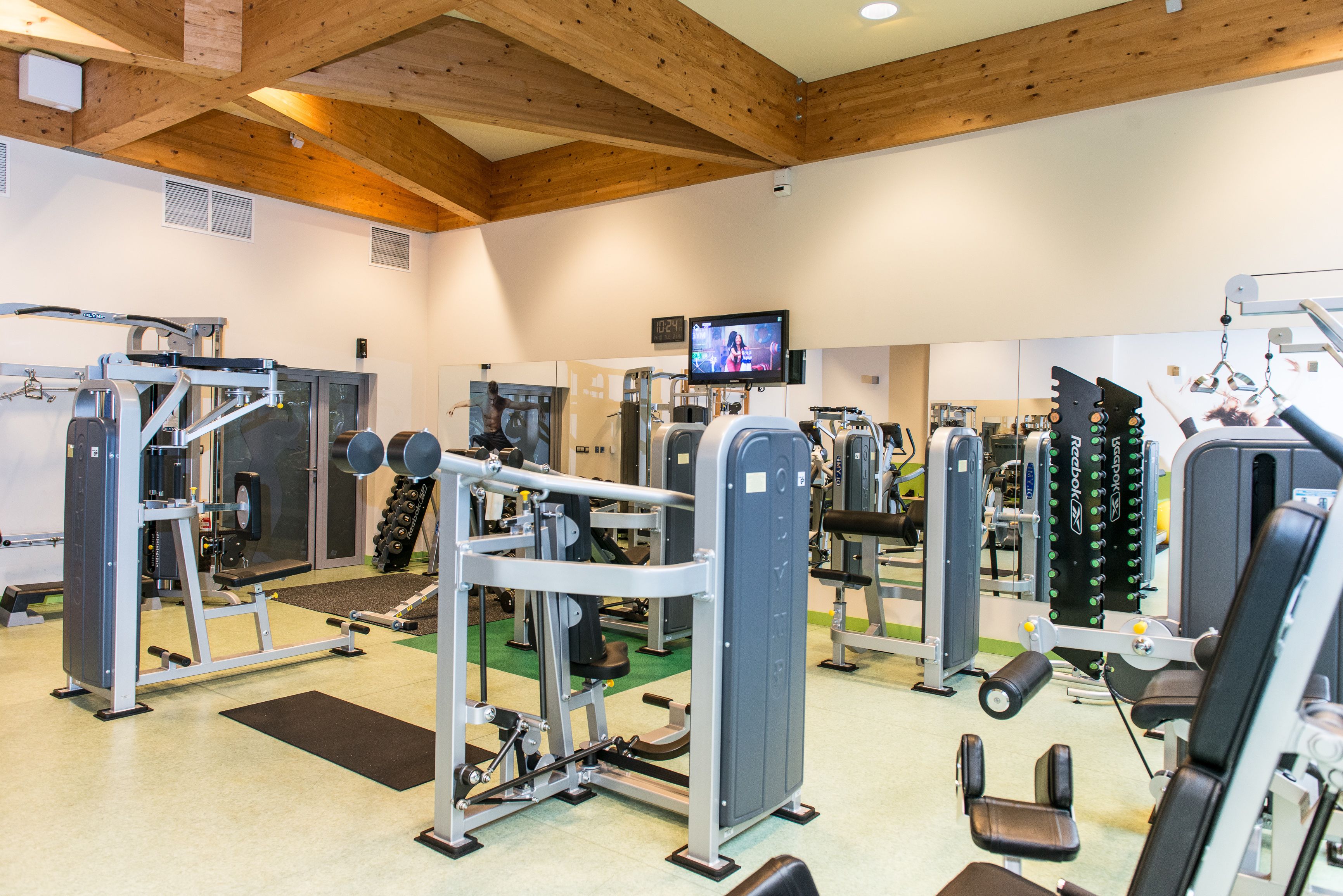 A gym with various exercise machines, a television screen, and wooden ceiling beams.