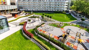 Un hotel moderno con un patio central, mobiliario exterior y un parque infantil.