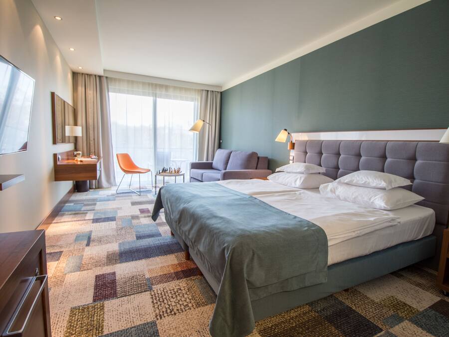 Ett hotellrum med en stor säng, ett skrivbord, en stol och en tv.