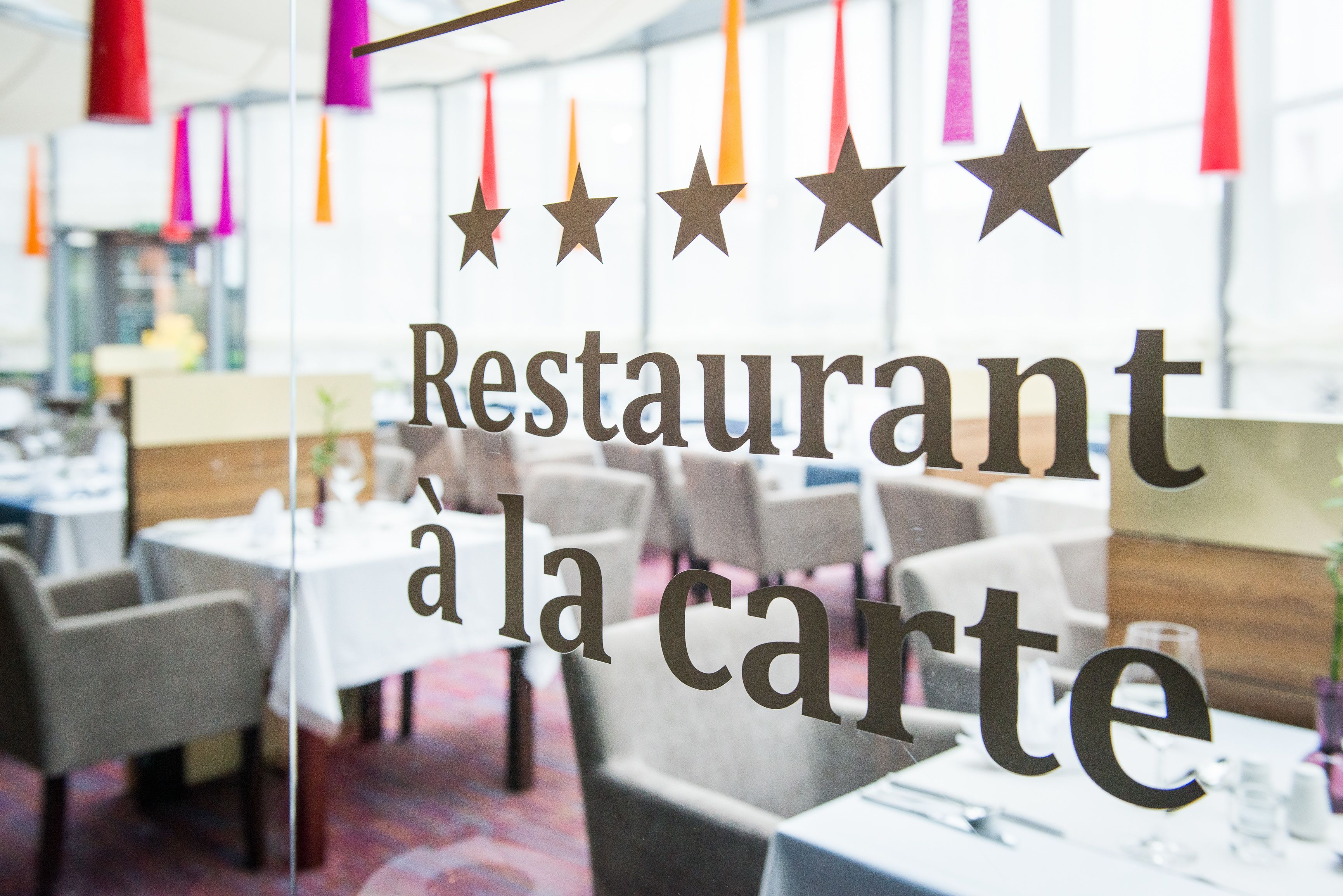 A restaurant interior with tables and chairs, a glass wall, and hanging decorations.
