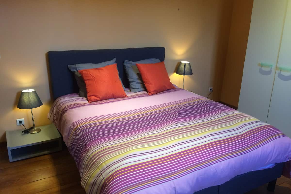 A bedroom with a bed, two bedside lamps, and a wardrobe.