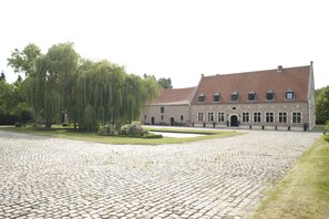 A large building with a tiled roof, a cobblestone courtyard, and a weeping willow tree. - Chapeauveau (Helecine)