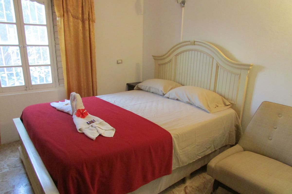 A bed with a red blanket, a white pillow, and a towel with a red flower.
