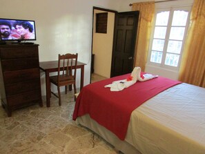 Una camera d'albergo con un letto, una scrivania, una sedia, una televisione e una porta.
