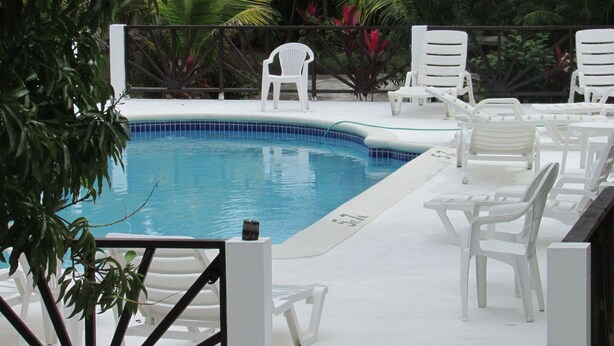 A swimming pool with white lounge chairs and a tiled deck. - Ocean Wave Villa (Negril)