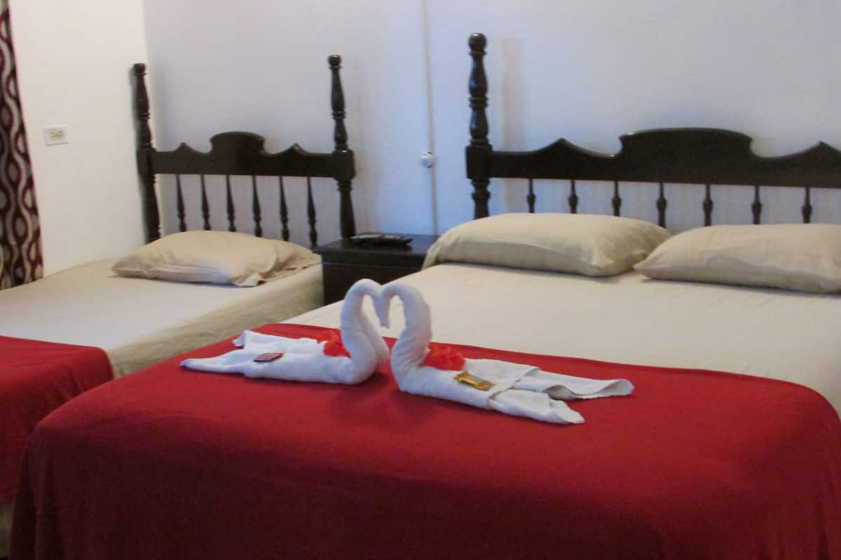 Two single beds with red bedspreads and wooden headboards, a nightstand with a remote control, and a decorative swan towel arrangement.
