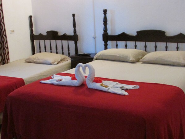 Due letti singoli con copriletto rosso e testate in legno, un comodino con telecomando e un’elegante composizione di asciugamani a forma di cigno.