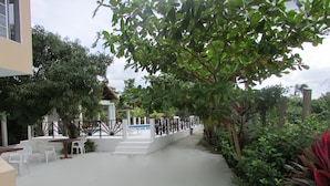 A pathway leading to a white building with a pool, surrounded by lush greenery and a fence. - Ocean Wave Villa (Negril)