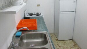 A compact kitchen with a sink, a stove, a microwave, and a refrigerator. - Ocean Wave Villa (Negril)