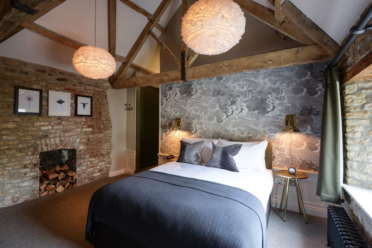 A bedroom with a large bed, a fireplace, and a rustic stone wall.
