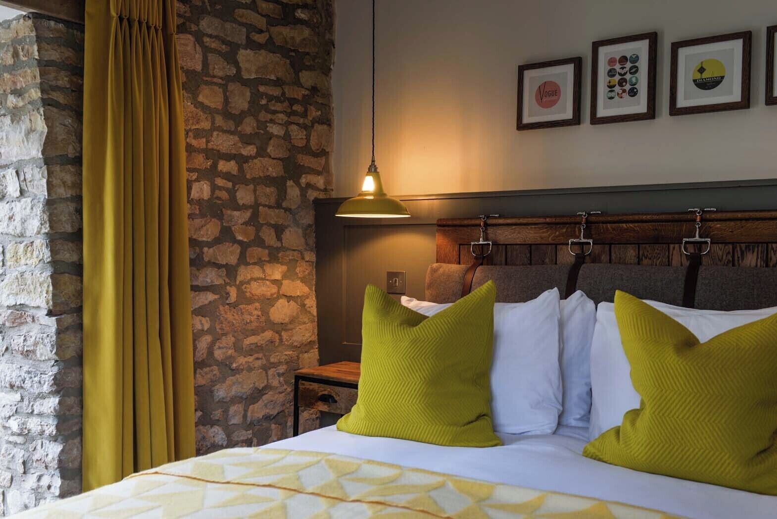 A hotel room with a stone wall, a bed with green and white pillows, a wooden headboard, and a hanging light fixture.