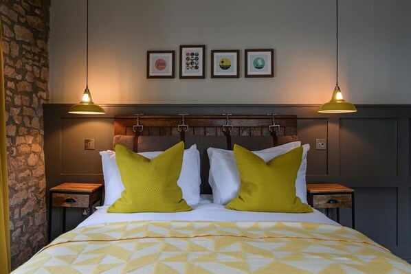 Habitación de hotel con cama, dos mesitas de noche, cabecero y cuatro cuadros enmarcados en la pared.