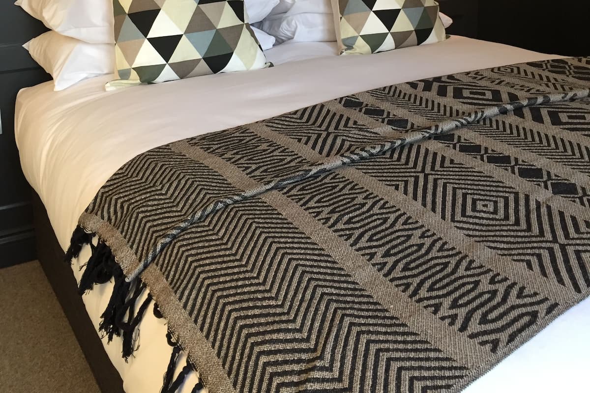 A neatly made bed with patterned pillows and a geometric throw blanket.