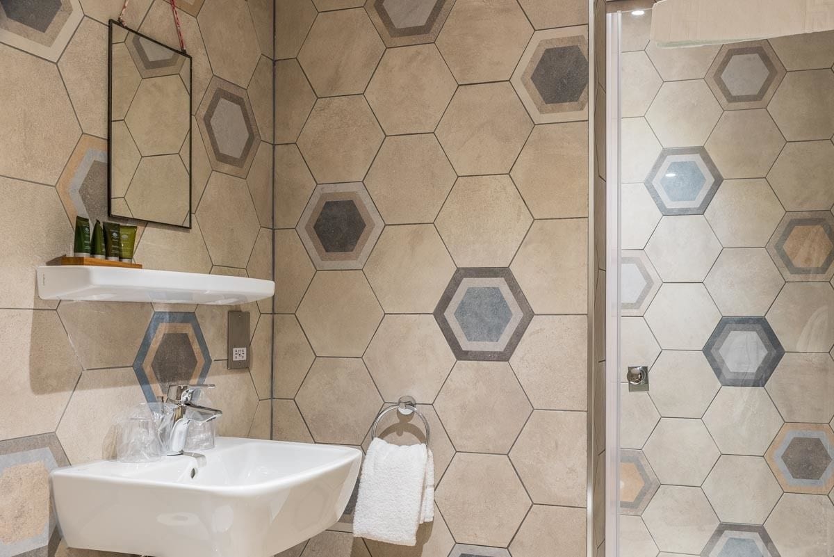 A bathroom with a hexagonal tile pattern, a white sink, a mirror, and a towel rack.