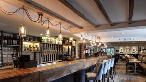 Zona de bar con mostrador de madera, lámparas colgantes y taburetes.