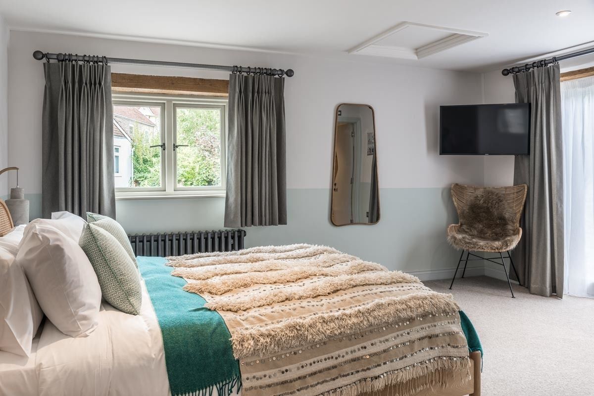 A bedroom with a bed, a chair, a TV, and a window with curtains.