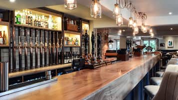 A bar area with a wooden bar counter, hanging light fixtures, and shelves with bottles.
