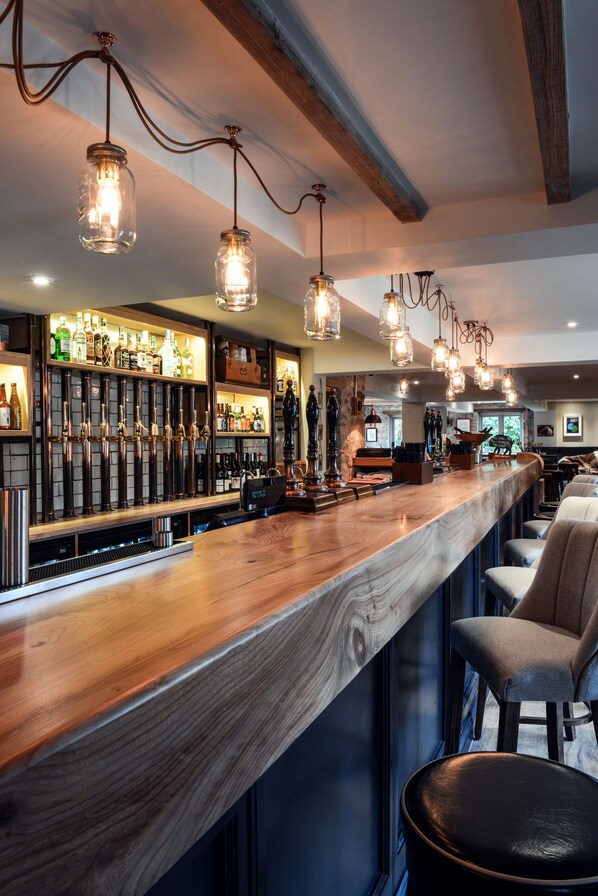 Zona de bar con mostrador de madera, lámparas colgantes y estantes con botellas.