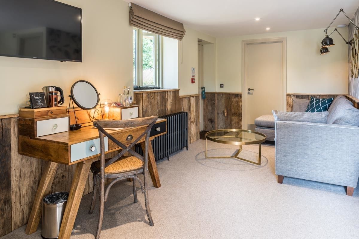 A cozy room with a wooden desk, a comfortable sofa, a TV mounted on the wall, and a window with curtains.