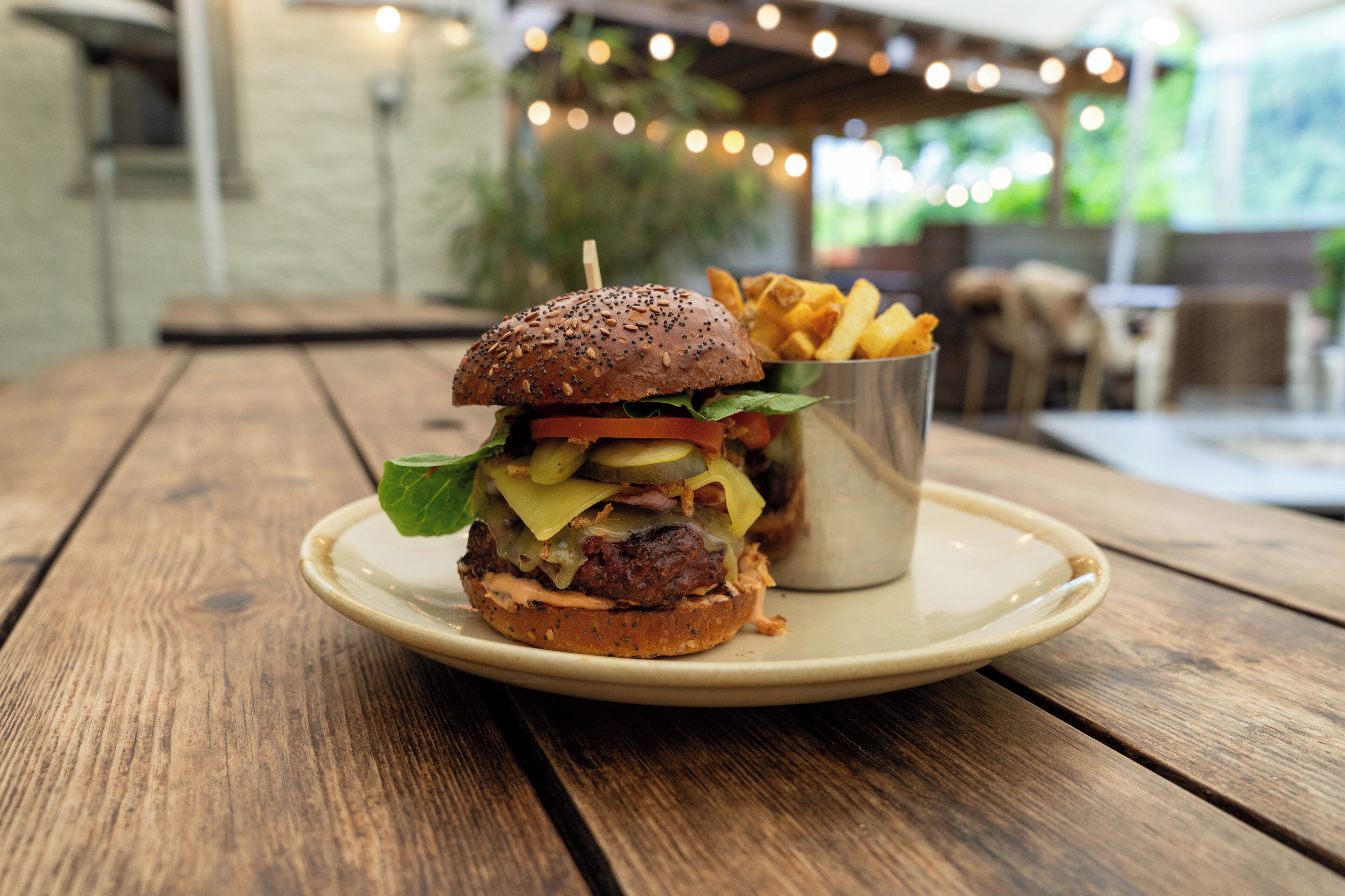 A burger with fries on a wooden table in an outdoor setting.
