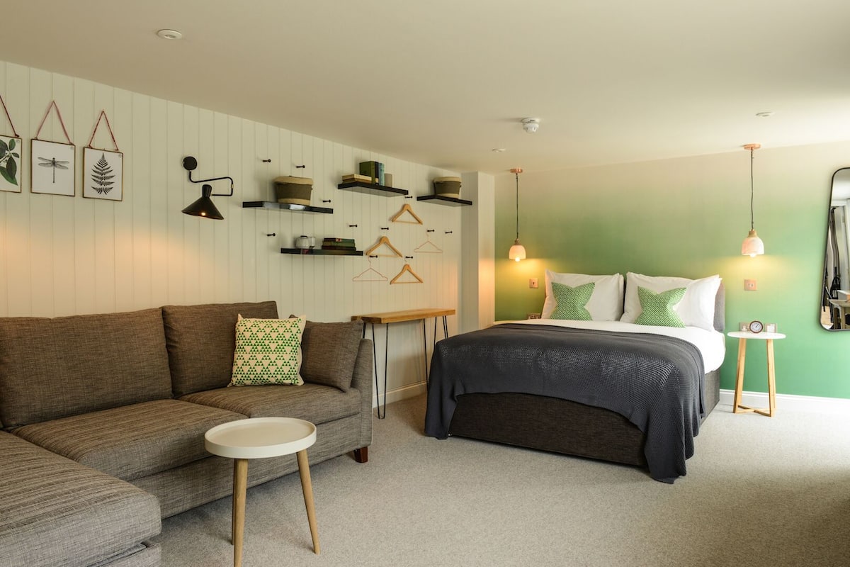 A bedroom with a bed, a sofa, a small table, and wall-mounted shelves.