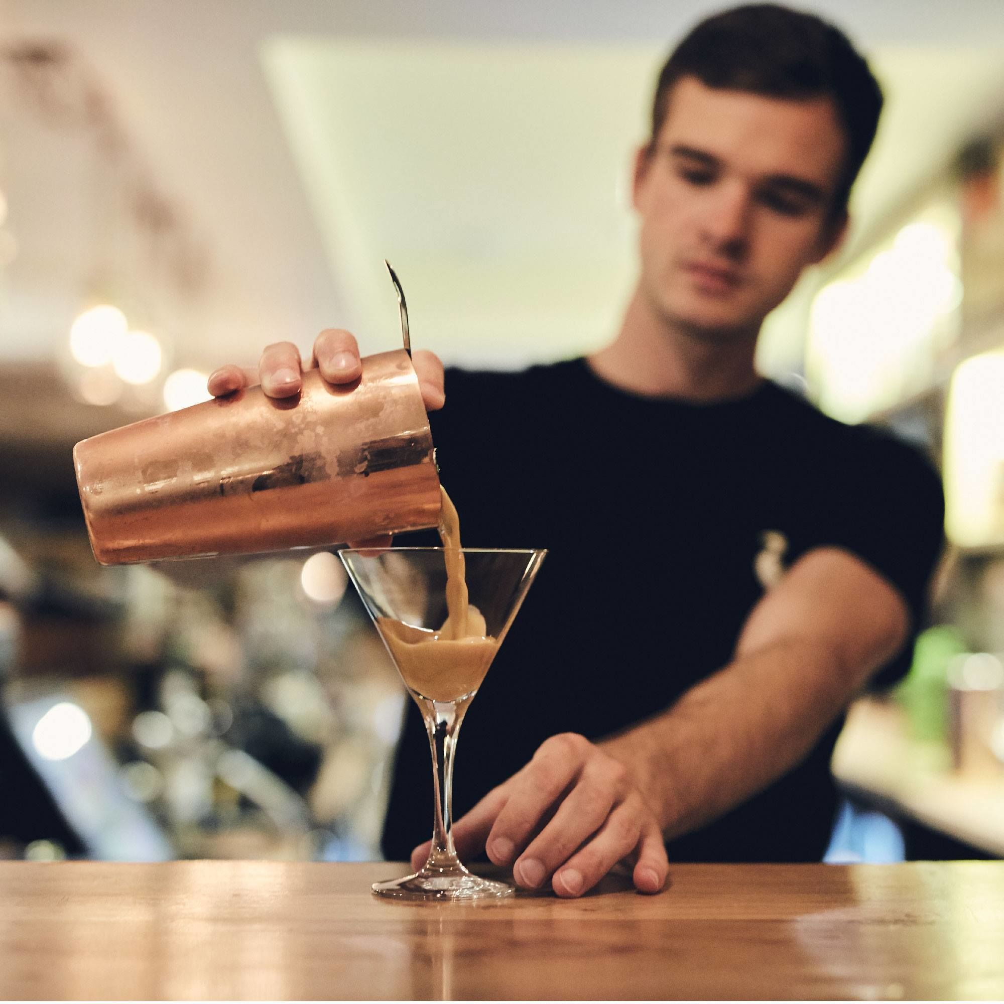A bartender pouring a drink into a martini glass.