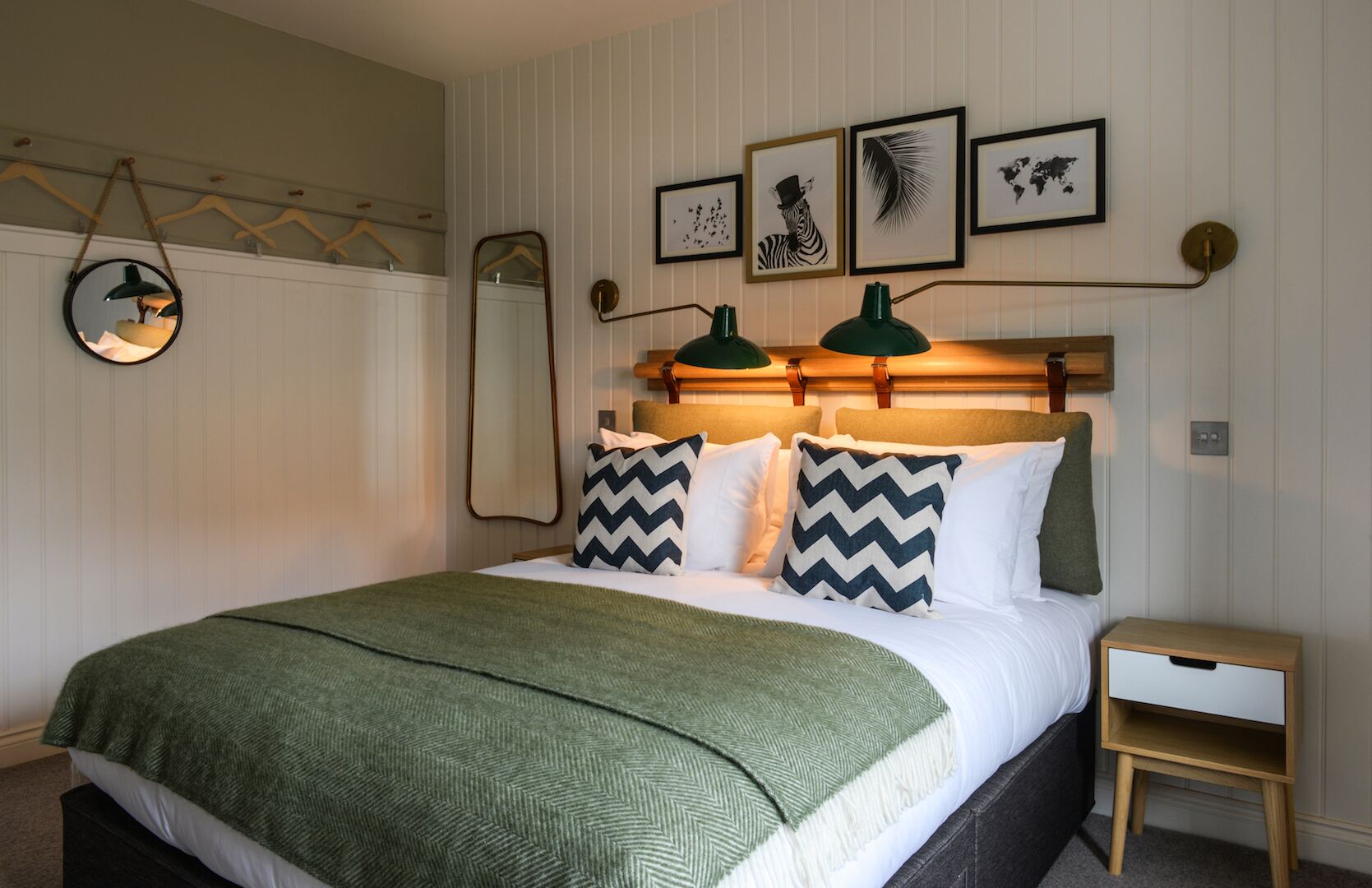 A neatly made bed with a green blanket, two pillows with zigzag patterns, and a bedside table with a lamp.