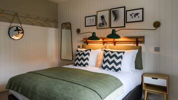 A neatly made bed with a green blanket, two pillows with zigzag patterns, and a bedside table with a lamp.