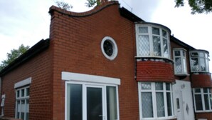 A red brick house with a white door and windows, a green trash bin, and a curved bay window.
