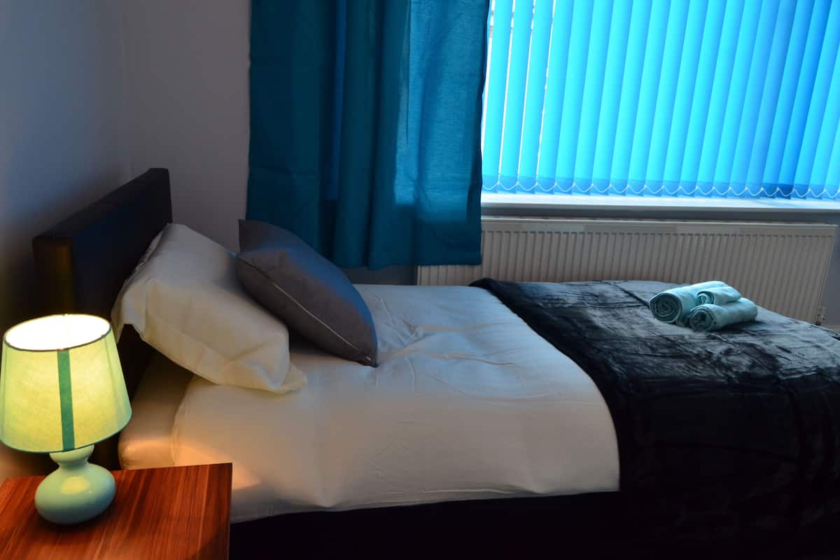 A neatly made bed with pillows, a bedside lamp, and a rolled towel on the bed.