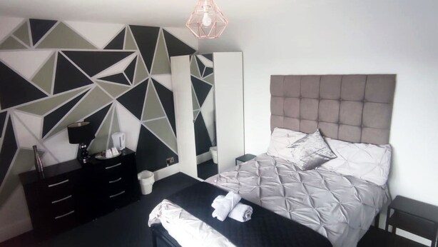 A modern bedroom with a geometric-patterned wall, a tufted headboard, and a neatly made bed with folded towels.