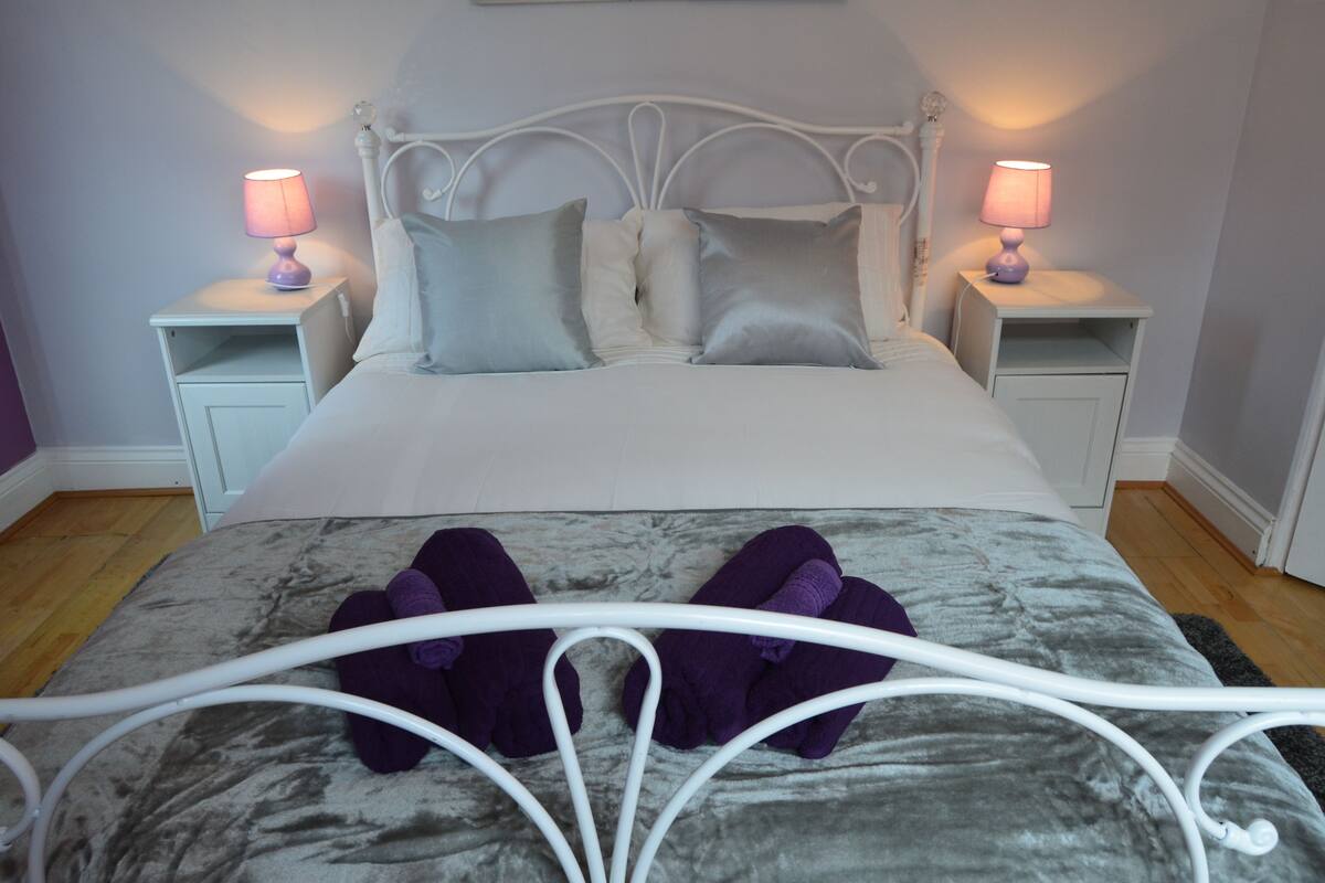 A neatly made bed with a grey and white duvet, two bedside tables with lamps, and a metal headboard.
