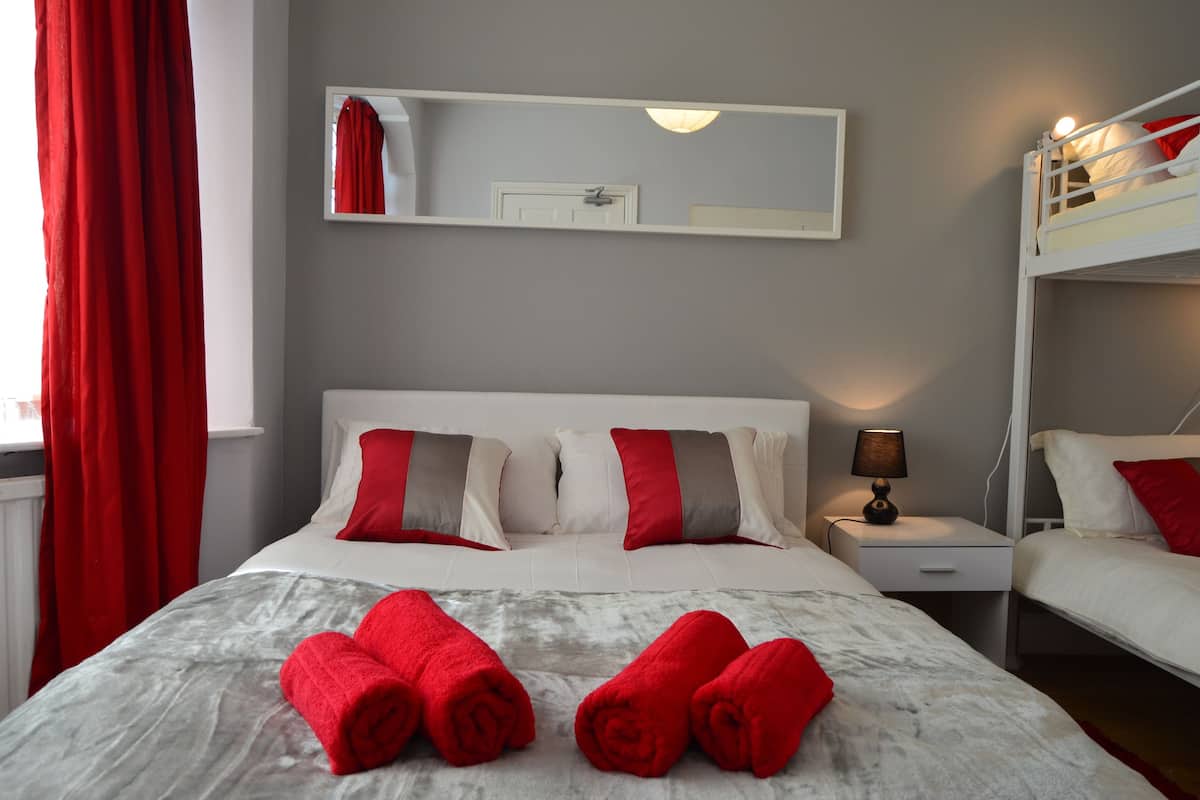 A hotel room with a bed, a nightstand, a lamp, a mirror, and a window with red curtains.